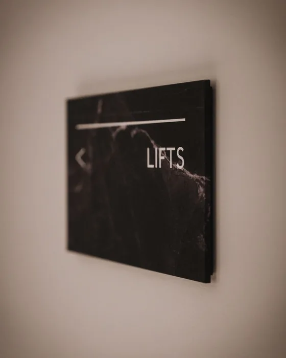 A dark marble directional sign on a wall, pointing to the lifts.