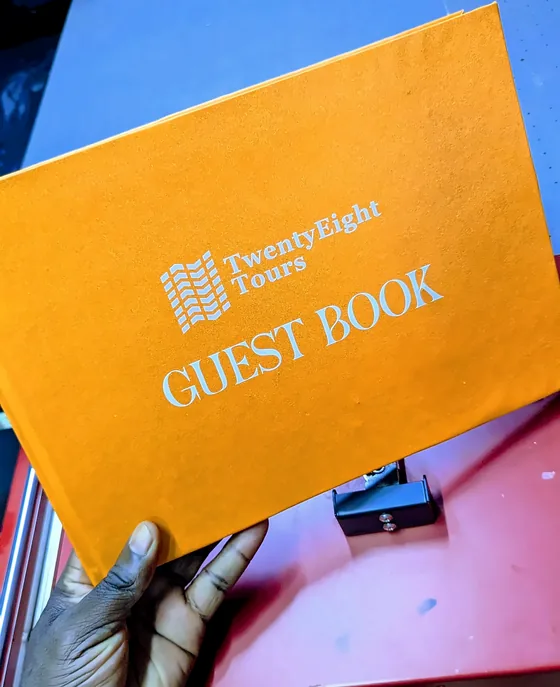 Orange Twenty Eight Tours guest book with a foiled cover, held in a hand.